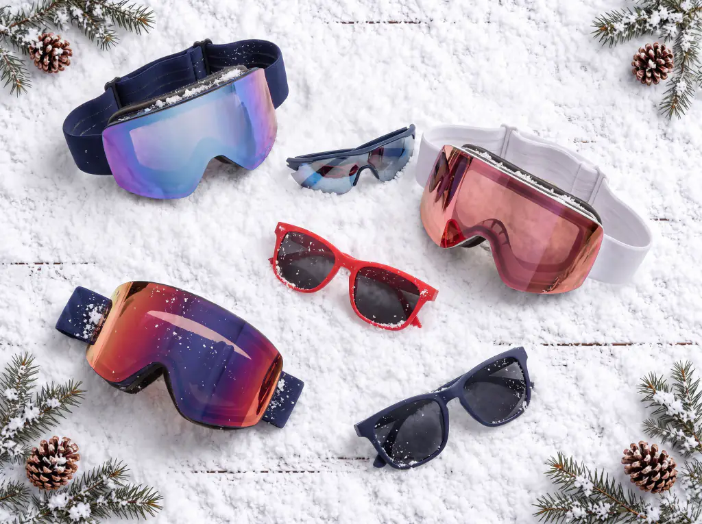 Three pairs of mirrored ski goggles and three pairs of sunglasses laid out on snow